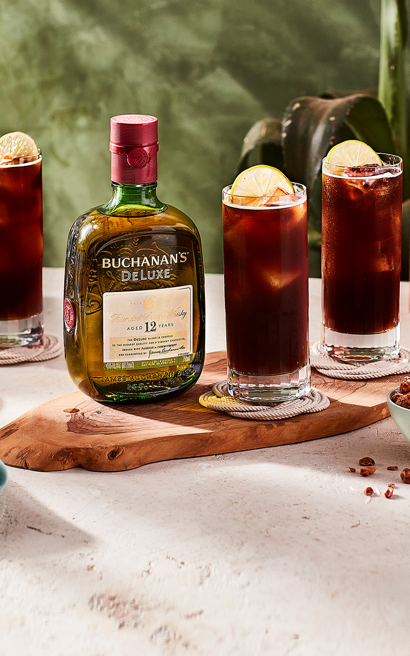 Three Buchandito cocktails sitting on a table around a bottle of Buchanan's Deluxe