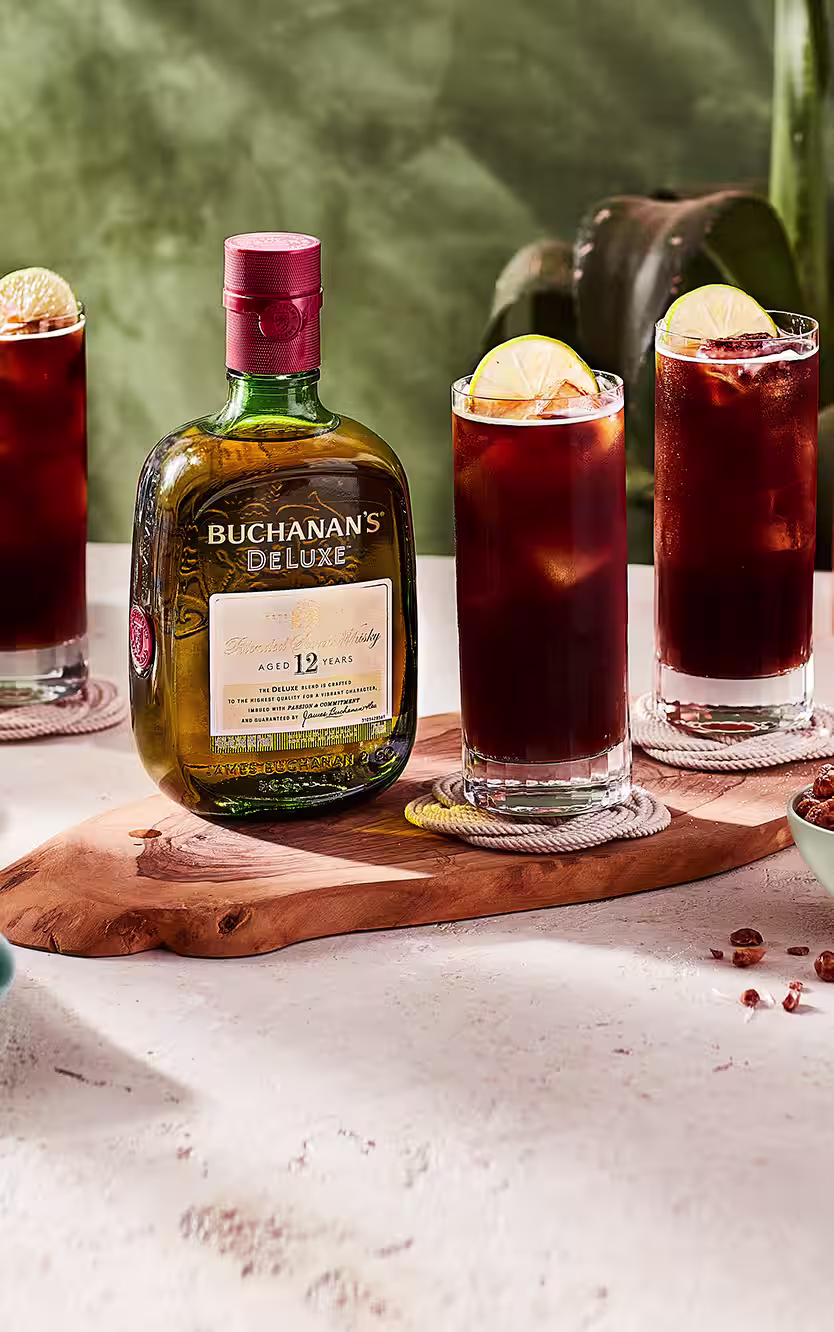 Three Buchandito cocktails sitting on a table around a bottle of Buchanan's Deluxe