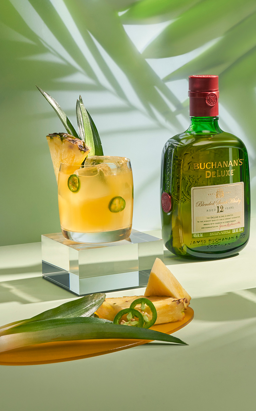 Two spicy piña margarita cocktails with a bottle of Buchanan's Deluxe in between the cocktails