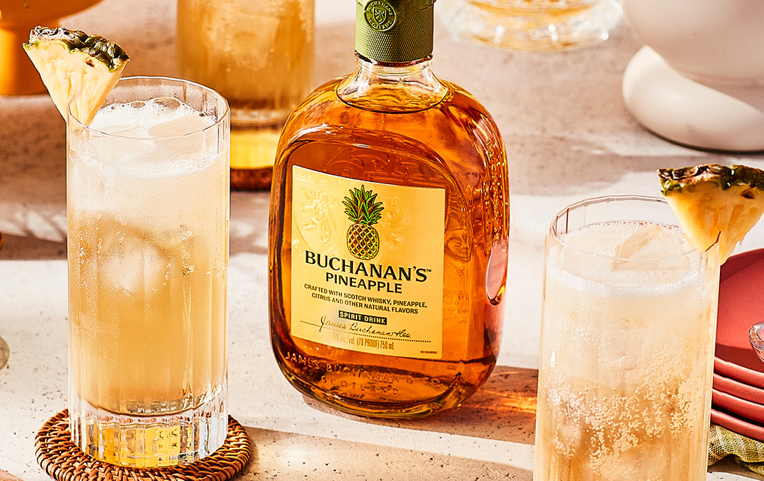 A bottle of Buchanan's Pineapple positioned between two Piña Fizz drinks on a counter