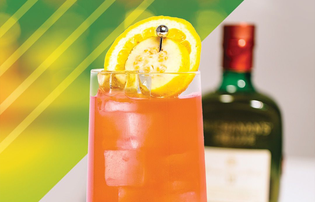 The Buchanan's La Familia cocktail garnished with a lemon slice. A bottle of Buchanan's Deluxe is blurred in the background. 