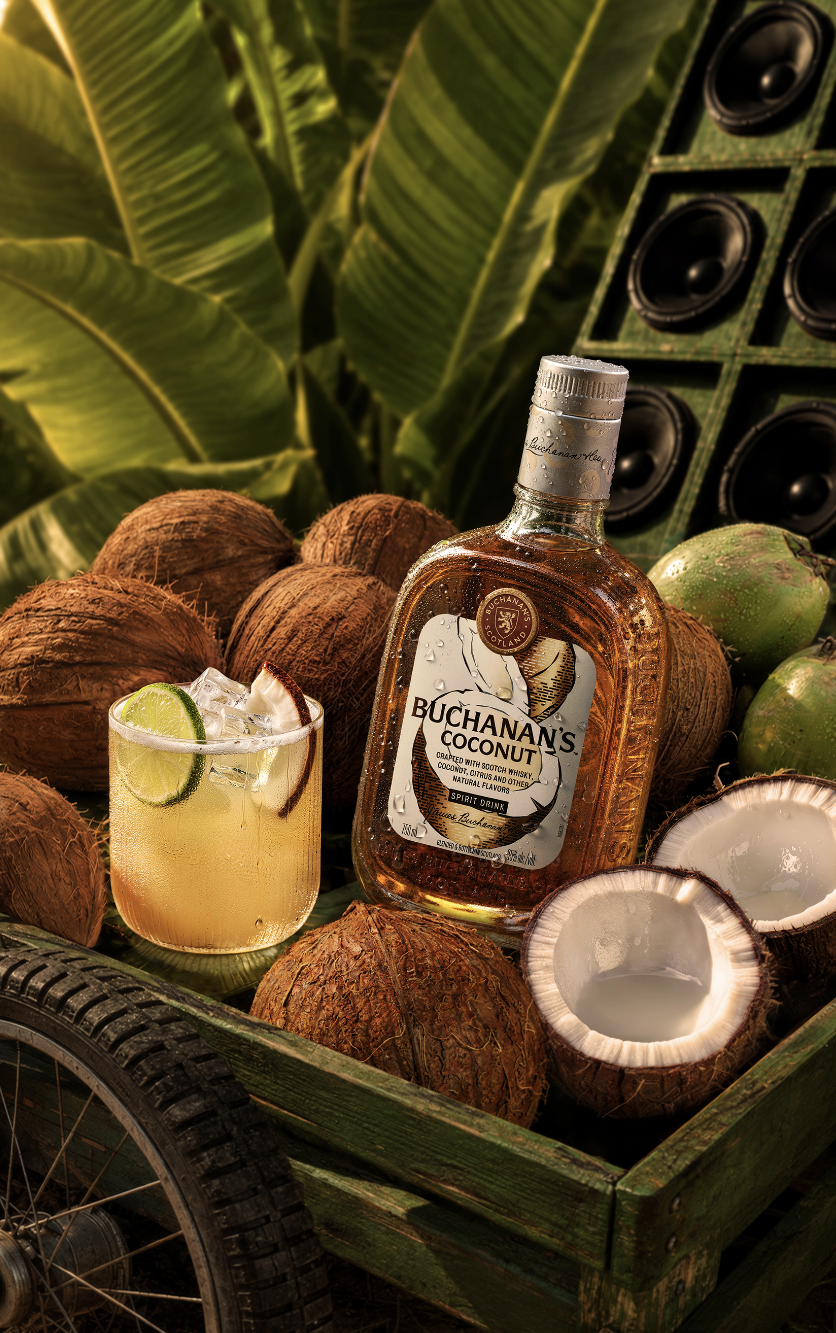 A Coco Sour cocktail on the rocks, garnished with a coconut chunk and slice of lime surrounded by coconuts.