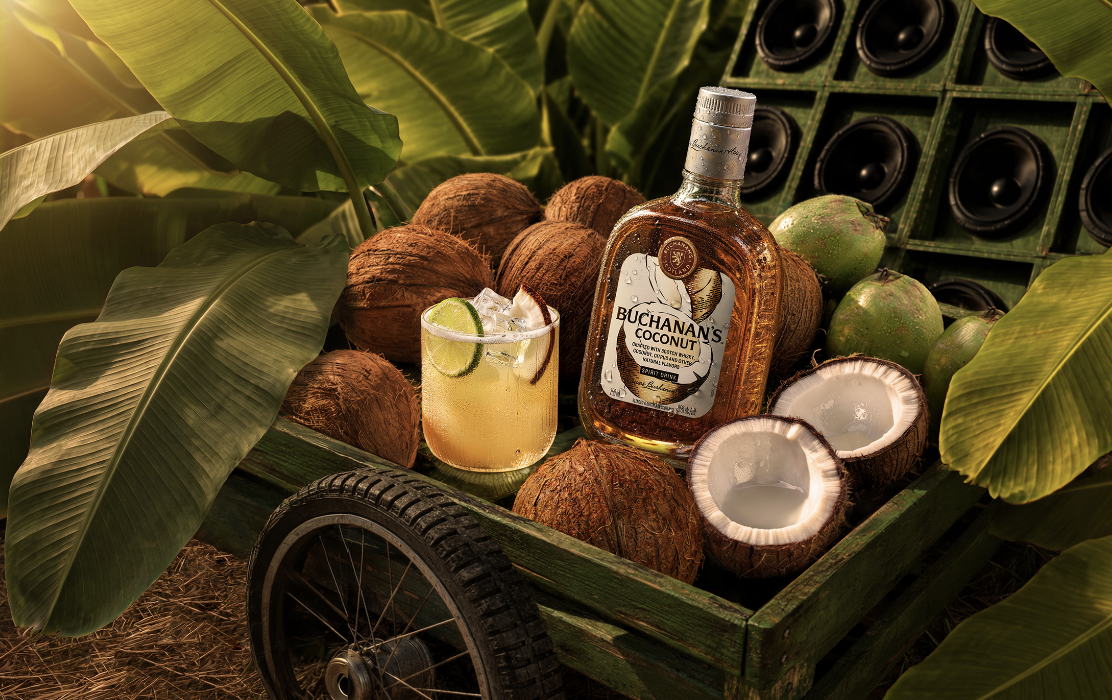 A Coco Sour cocktail on the rocks, garnished with a coconut chunk and slice of lime surrounded by coconuts.