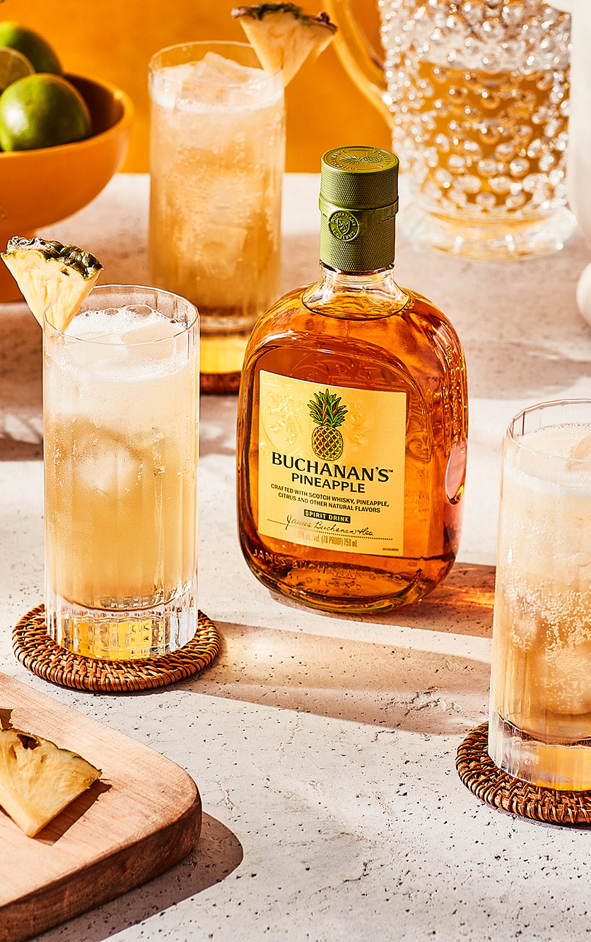 A bottle of Buchanan's Pineapple positioned between two Piña Fizz drinks on a counter