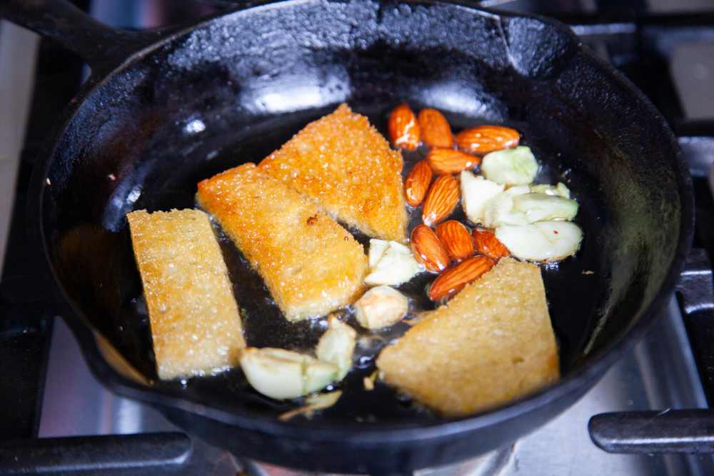 1. In a small skillet, heat 2 tablespoons olive oil over medium high heat. Add almonds, bread, and garlic and toast. 