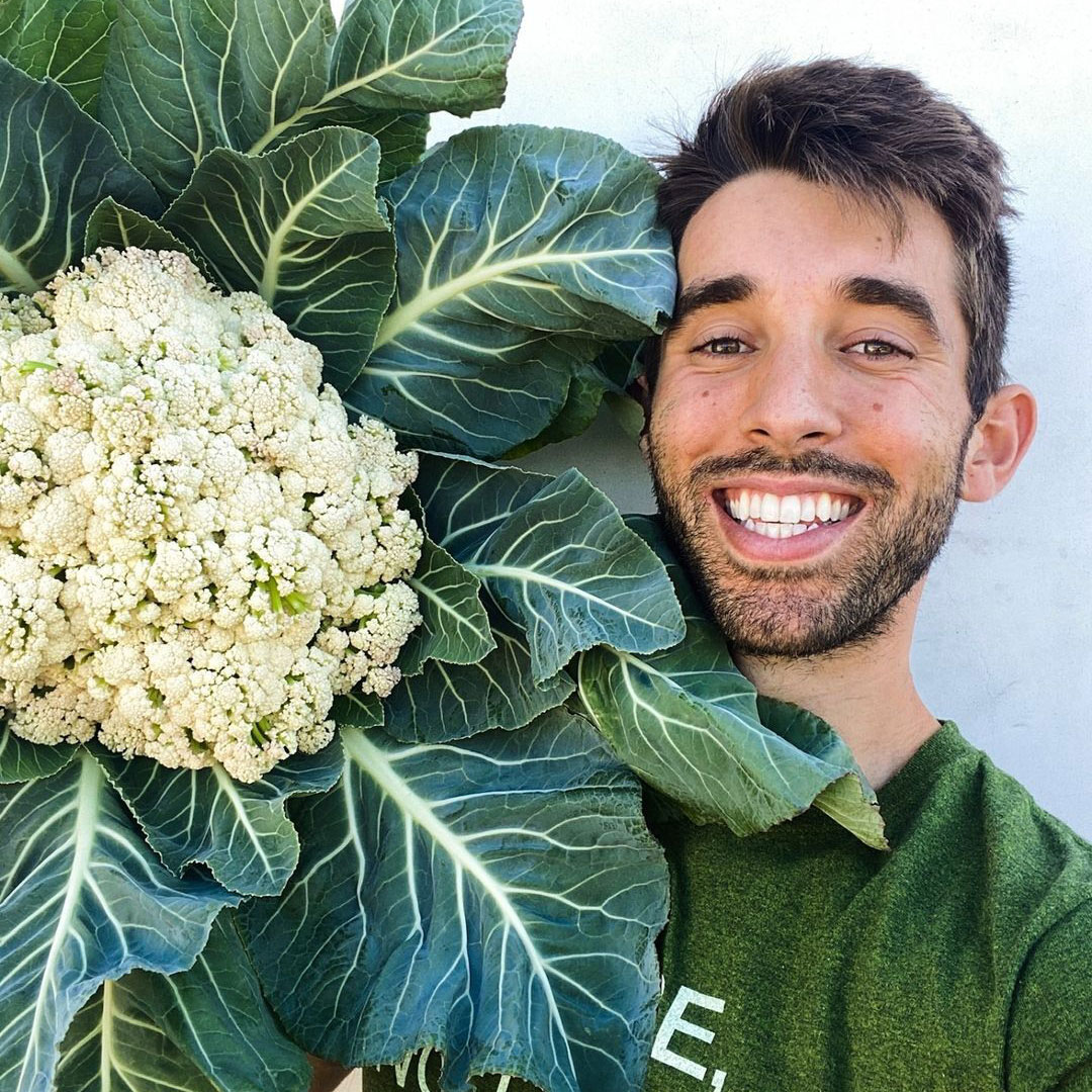 A man smiling and holding a large cauliflower.