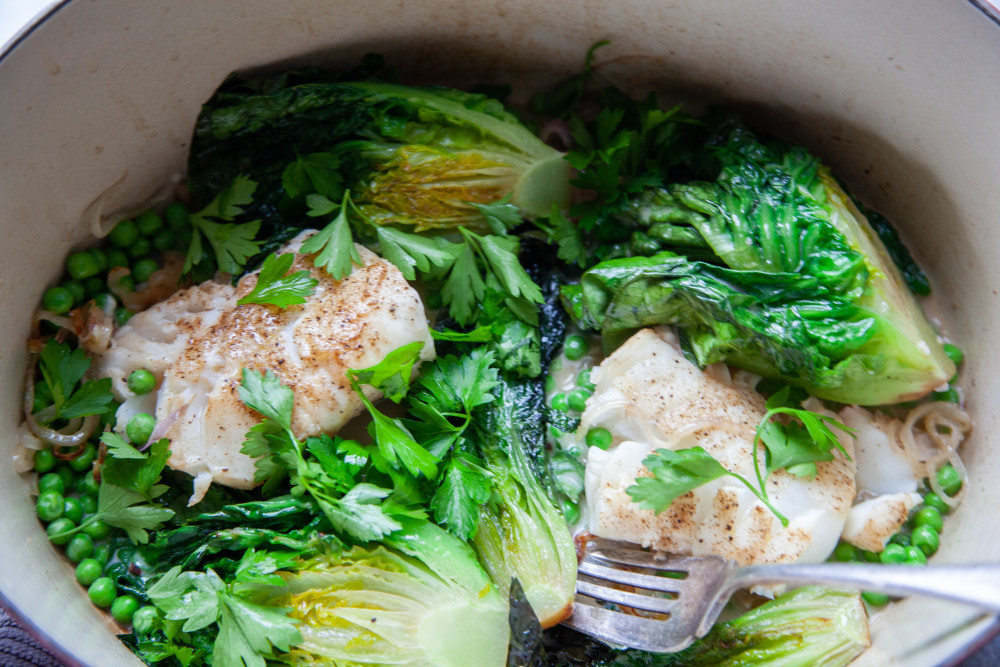 Add lettuce heads to pan, cut side down, and cook until they are slightly browned. Return fish filets to the pan, nestling between the lettuce, and distribute frozen peas around lettuce and fish. 