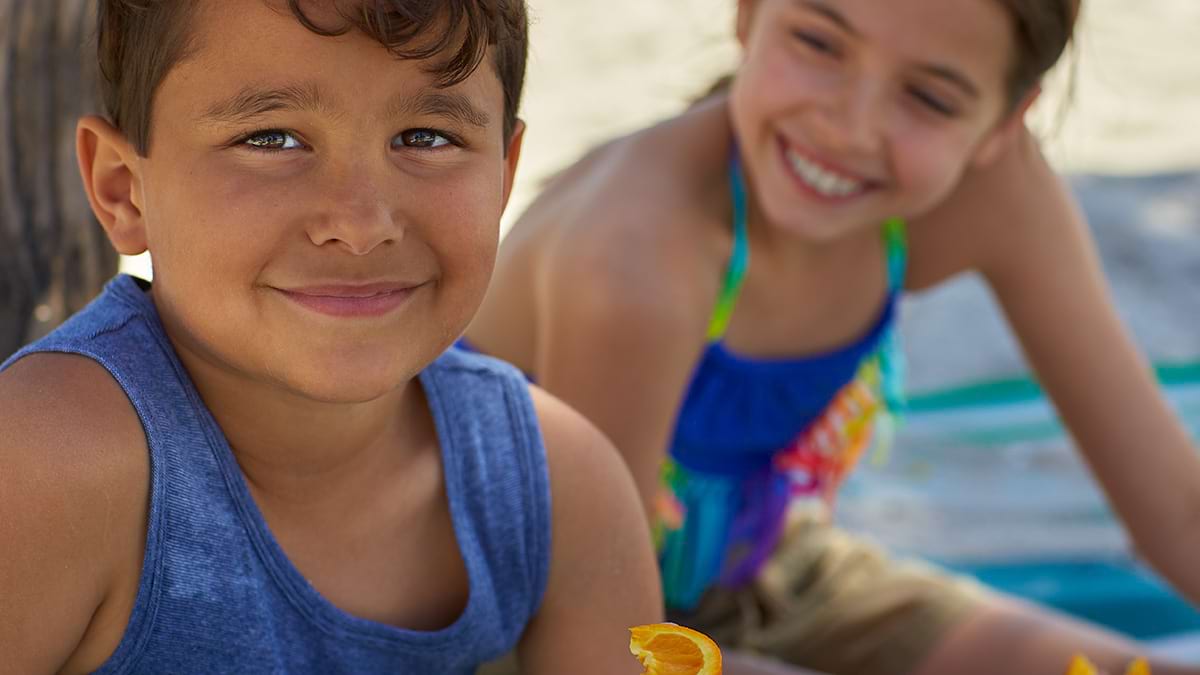 Two children sitting on the beach. They are both smiling. 