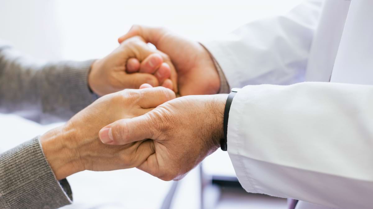 A health care professional holding the hands of a patient.