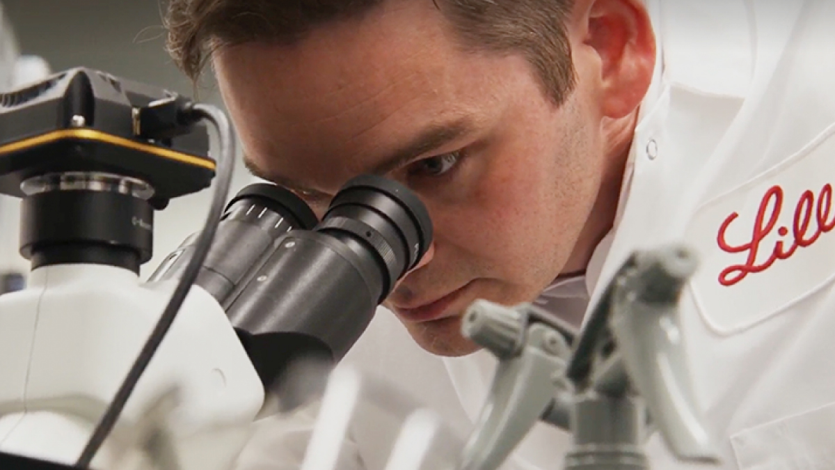 Person in a Lilly lab coat looking into a microscope. 