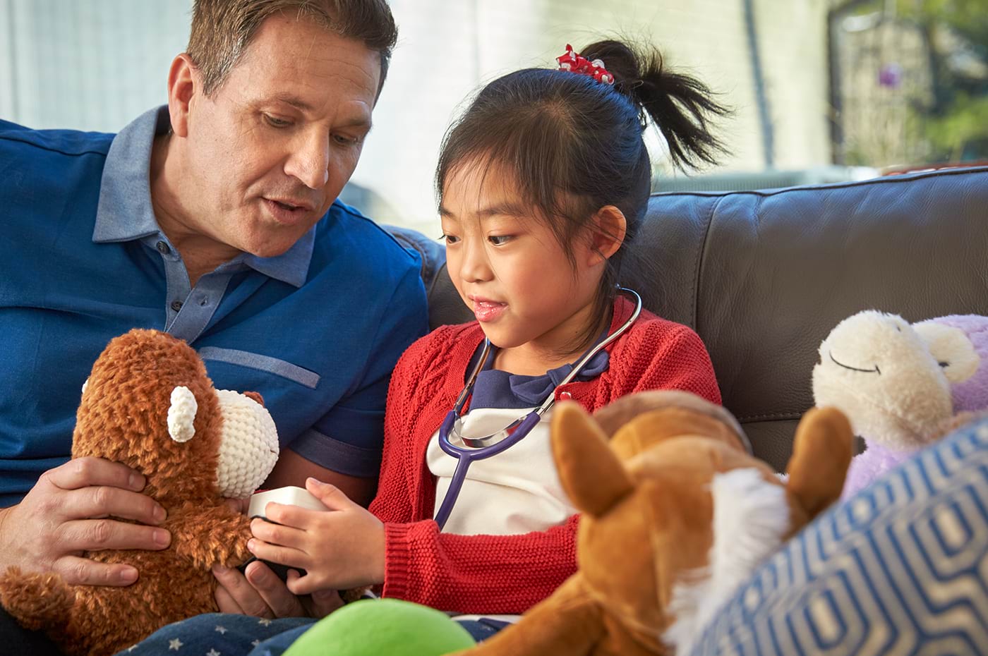 An adult holding a teddy bear and playing with a child who has a stethoscope.  
