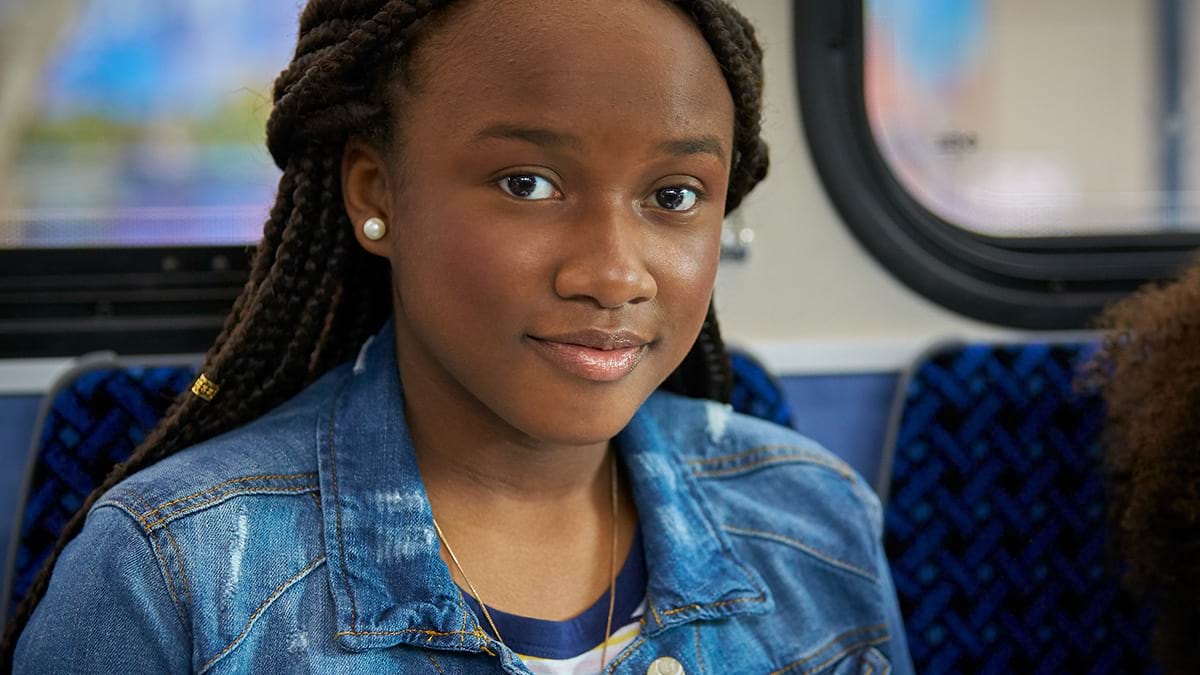 A child sitting on public transport. They are wearing a denim jacket and smiling at the camera. 