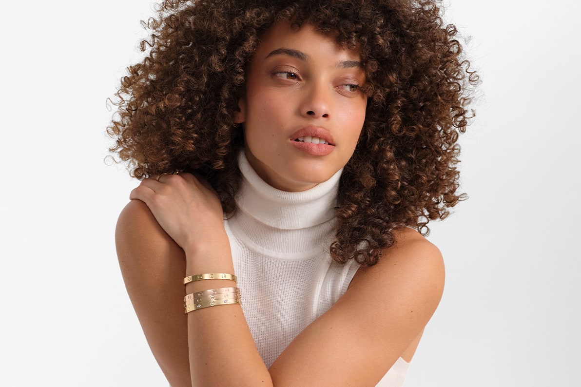 a woman wearing a white sleeve turtleneck dress and a stack of yellow gold Cartier Love bracelets on her arm