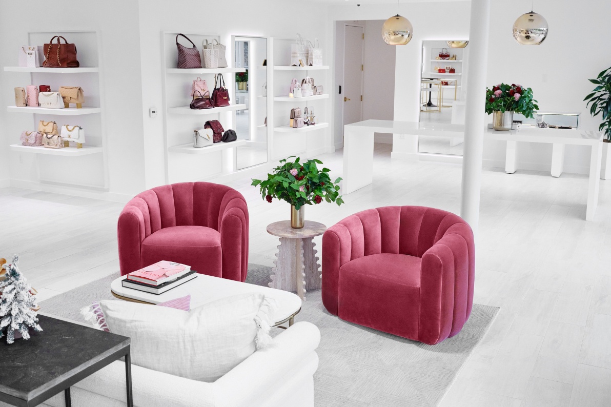 the interior of the San Diego Flagship viewing two dark pink upholstered chairs with a small side table in between and a white sofa with various designer bags displayed on the walls