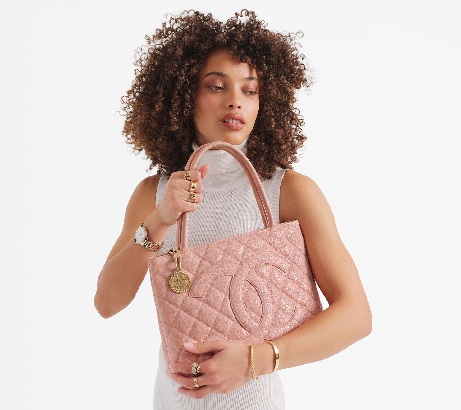 a woman in a white sleeveless sweater dress holding a pink Chanel Medallion tote