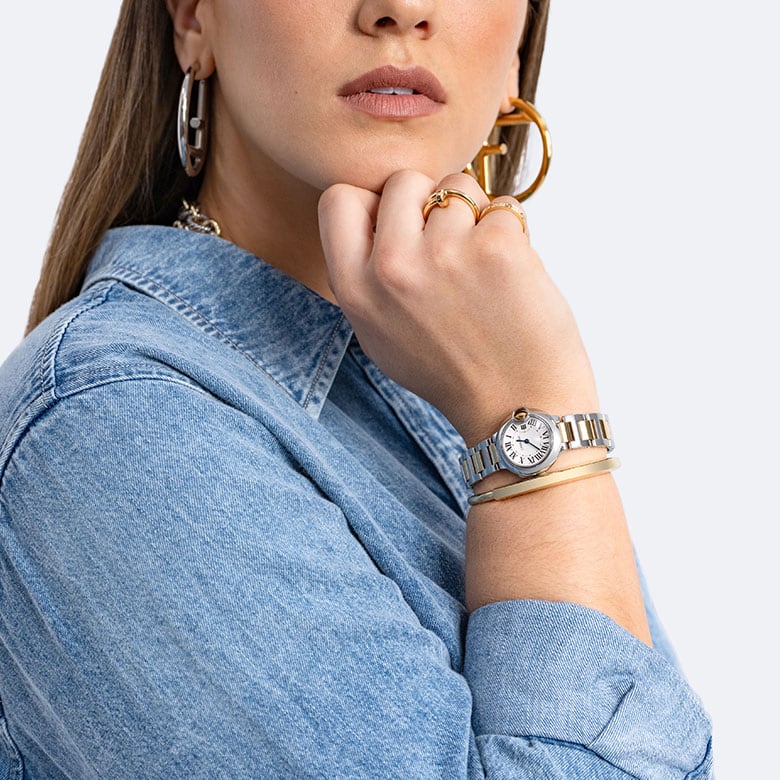 a woman wearing a denim shirt, silver and gold Fendi hoop earrings, a gold Tiffany Lock Bracelet and a Cartier Stainless Steel 18K Yellow Gold 28mm Ballon Bleu De Cartier Quartz Watch