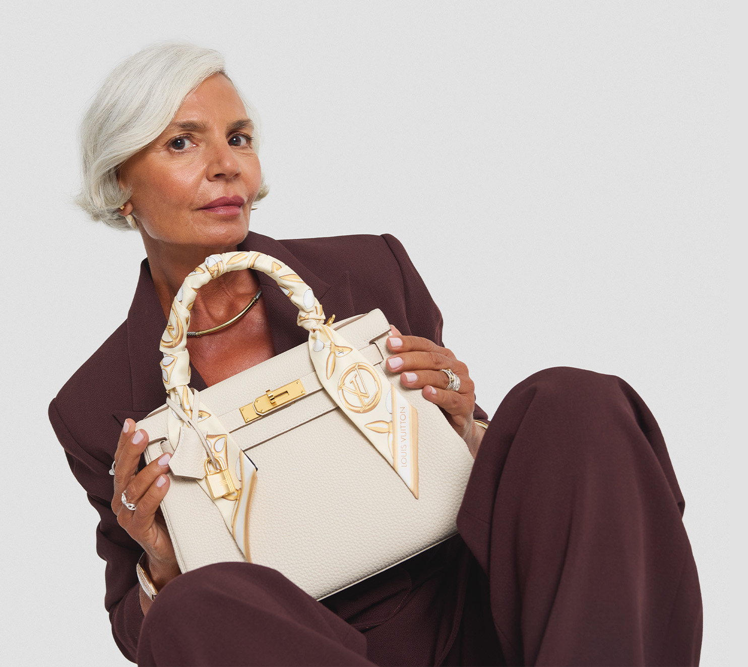 a woman in a brown suit holding a white Hermes Kelly with an Hermes twilly