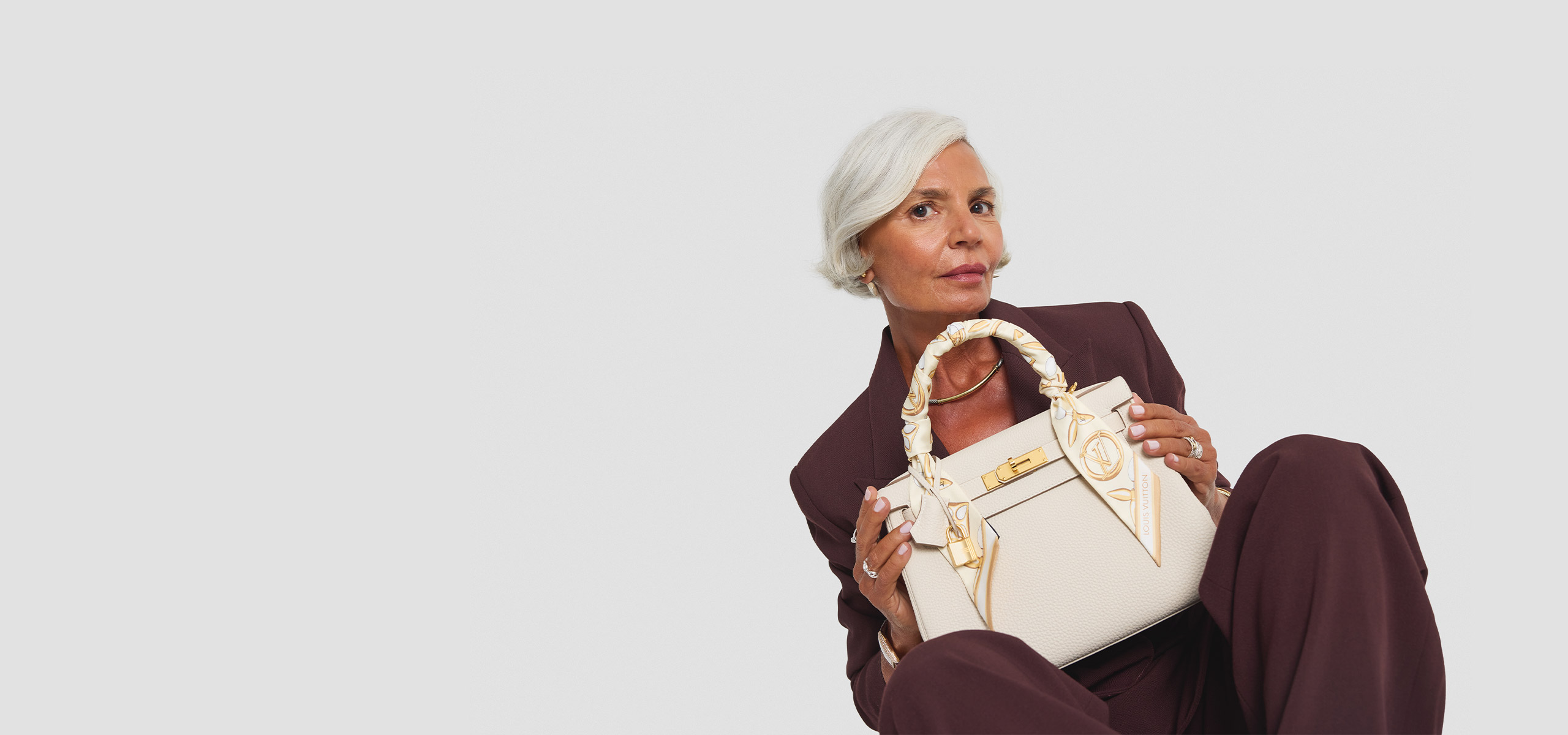 a woman in a brown suit holding a white Hermes Kelly with an Hermes twilly