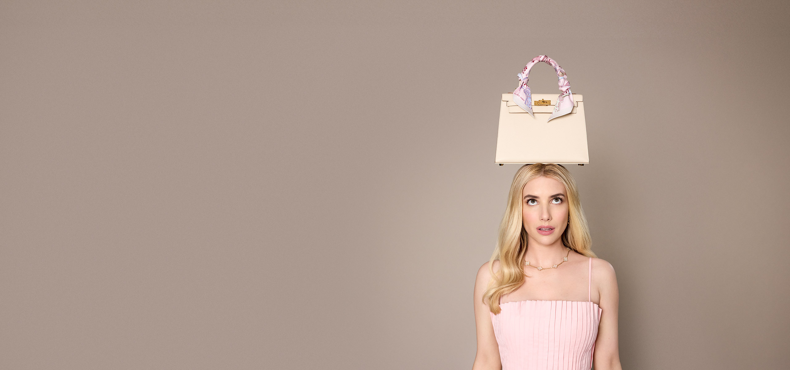 Emma Roberts in a pink dress with a white Hermes Kelly and an Hermes twilly wrapped around the handle sitting on her head