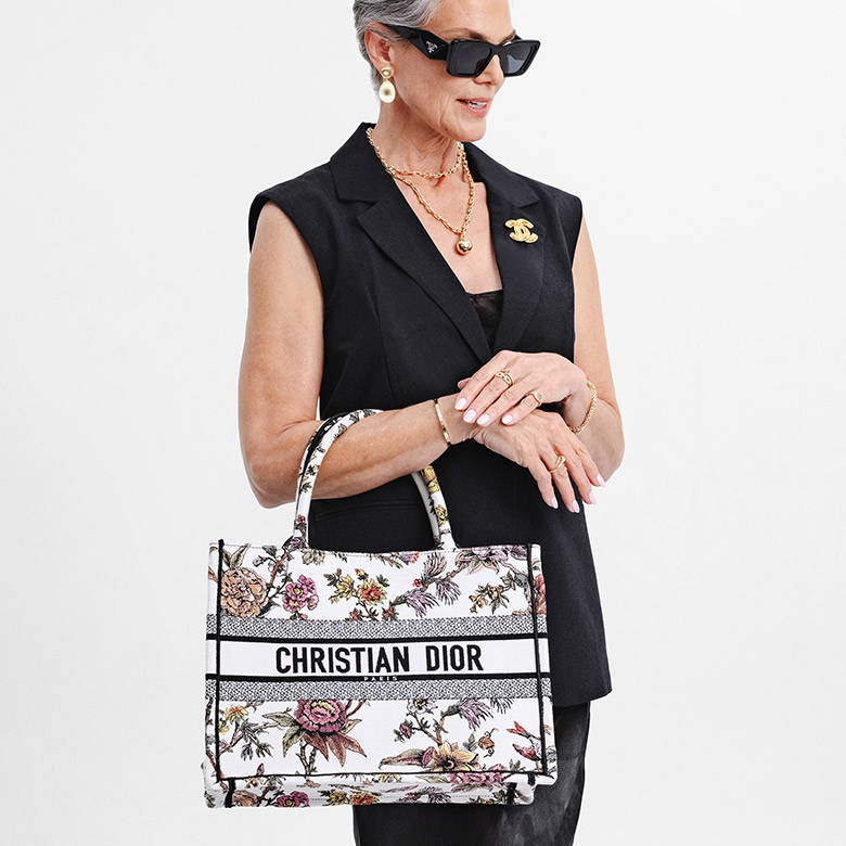 a woman in a black vest and black sunglasses holding a CHRISTIAN DIOR Canvas Embroidered Medium Rosa Mutabilis Book Tote