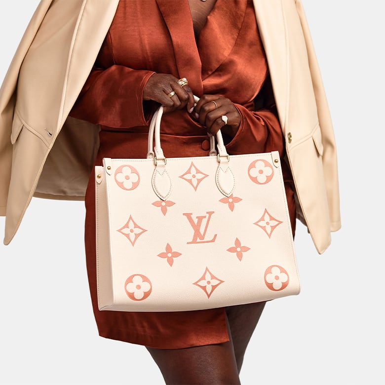 Woman in a bronze jumpsuit and beige blazer holding a LOUIS VUITTON Empreinte Monogram Giant Onthego MM in Creme Rose Trianon