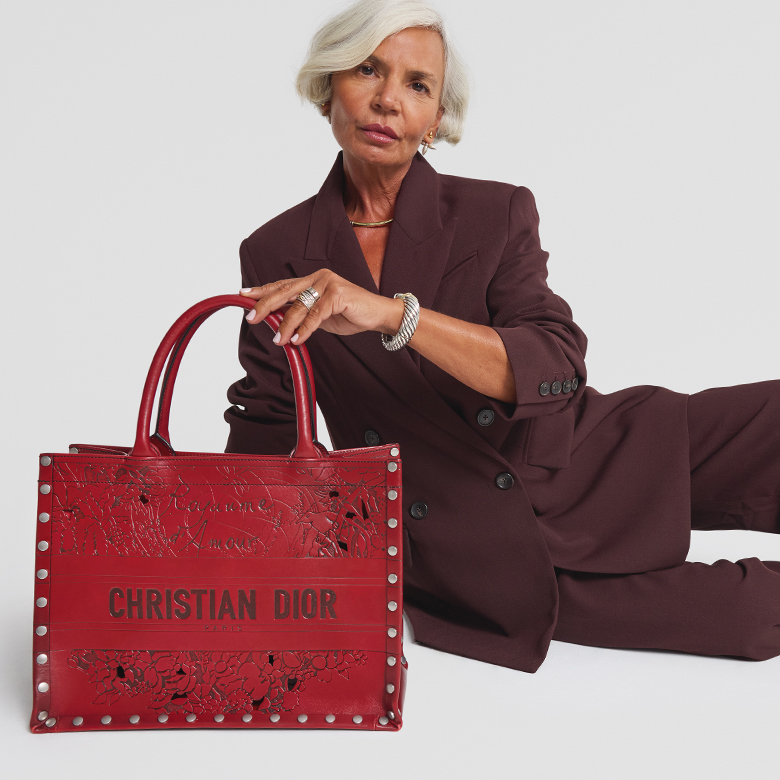 influencer Grece Ghanem wearing a matching burgundy color suit blazer and pants and sitting next to and holding a Christian Dior Calfskin Laser Cut Studded Medium Book Tote in Red