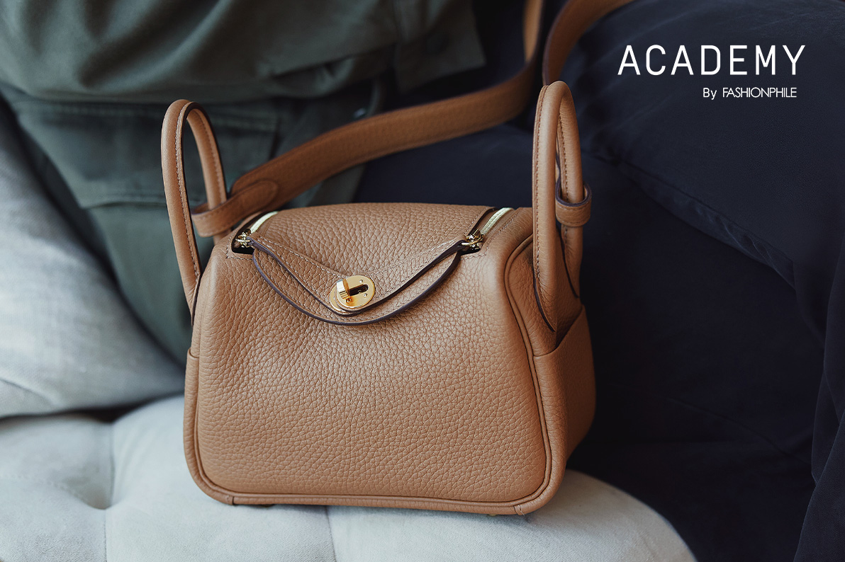 one brown Hermes Mini Lindy sitting on a couch next to a woman in a suit with "ACADEMY BY FASHIONPHILE" in white text