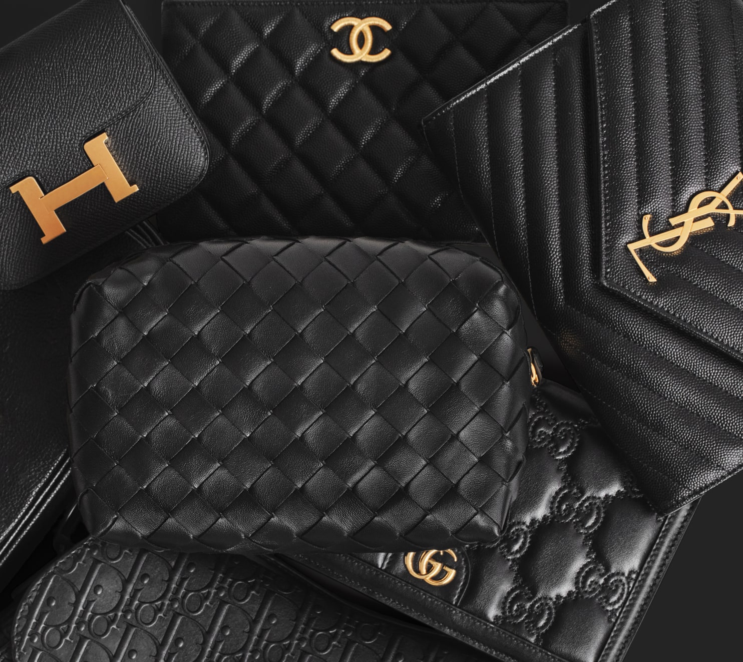 a group of black designer bags laid down - one black Louis Vuitton Pochette Metis bag, one black Hermes Constance compact wallet, one black Bottega Veneta pouch and one black Saint Laurent Chevron Quilted Envelope bag