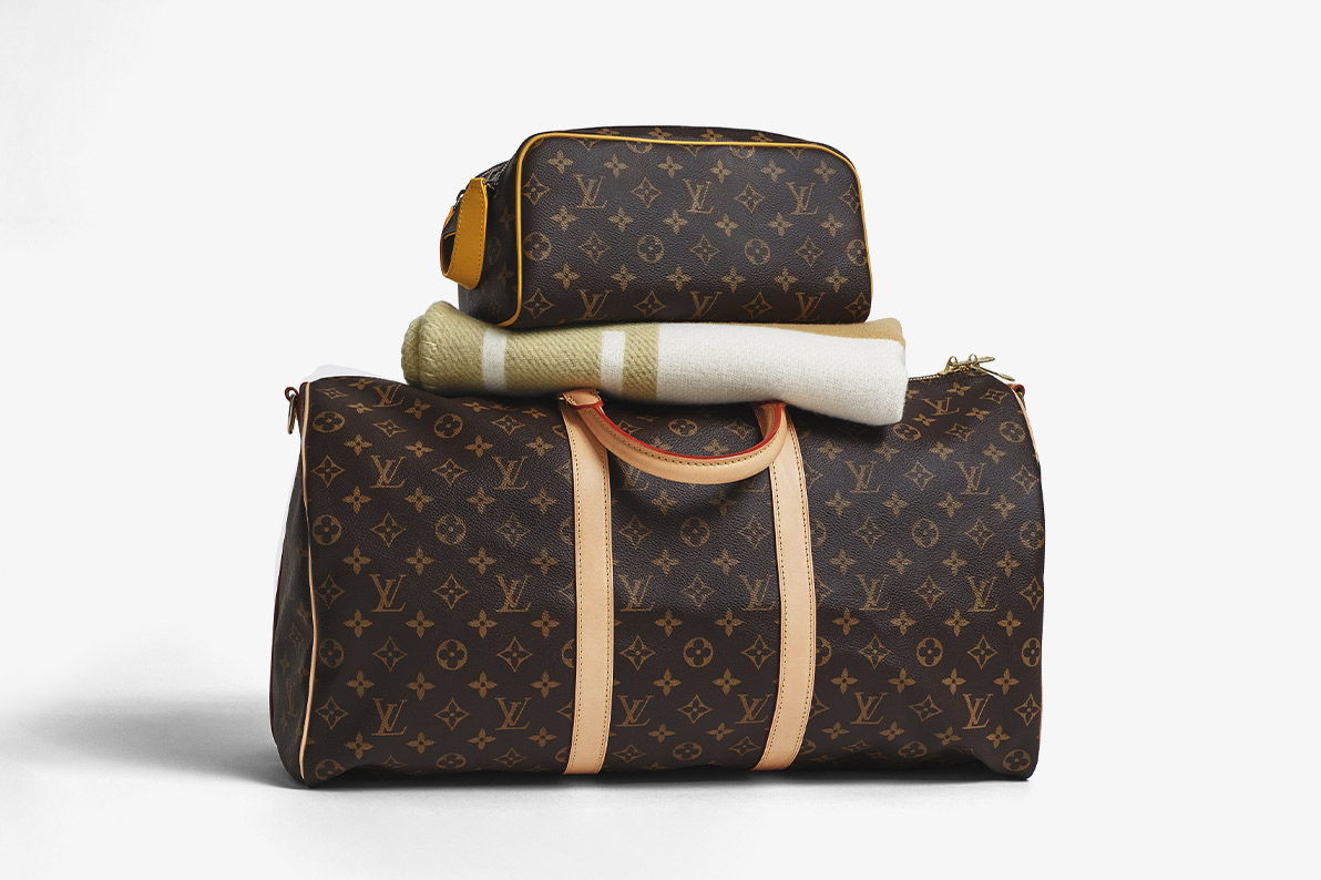 one LOUIS VUITTON Monogram Keepall 50 with an HERMES Wool Cashmere Avalon Baby Blanket and one LOUIS VUITTON Monogram King Size Toiletry Bag on top of it