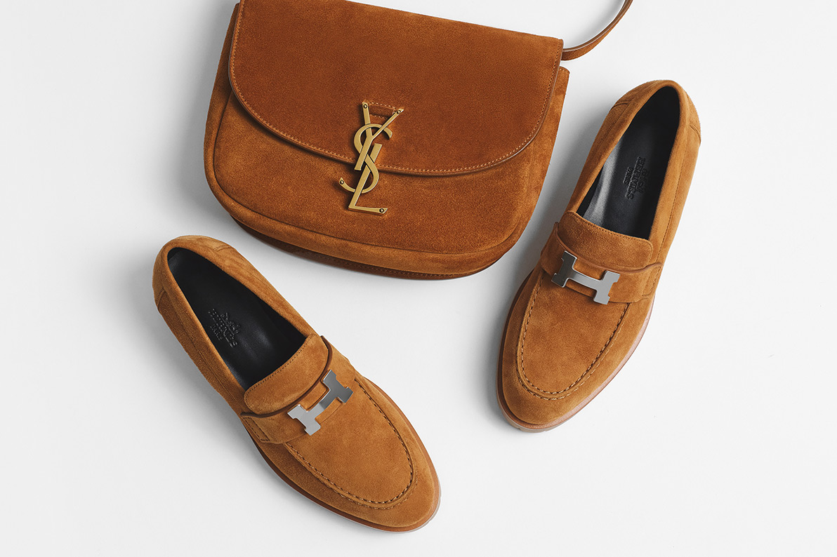 one pair of brown HERMES Suede Goatskin Paris Loafers sitting next to one SAINT LAURENT Suede Calfskin Monogram Medium Kaia Satchel Light Cinnamon