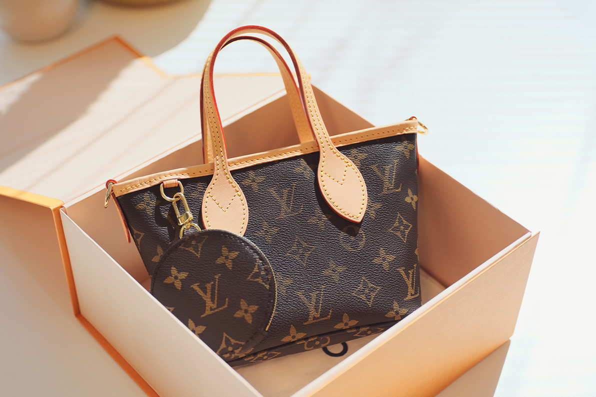 a Louis Vuitton Monogram Neverfull tote in the BB size sitting in an orange Louis Vuitton brand box with the lid open