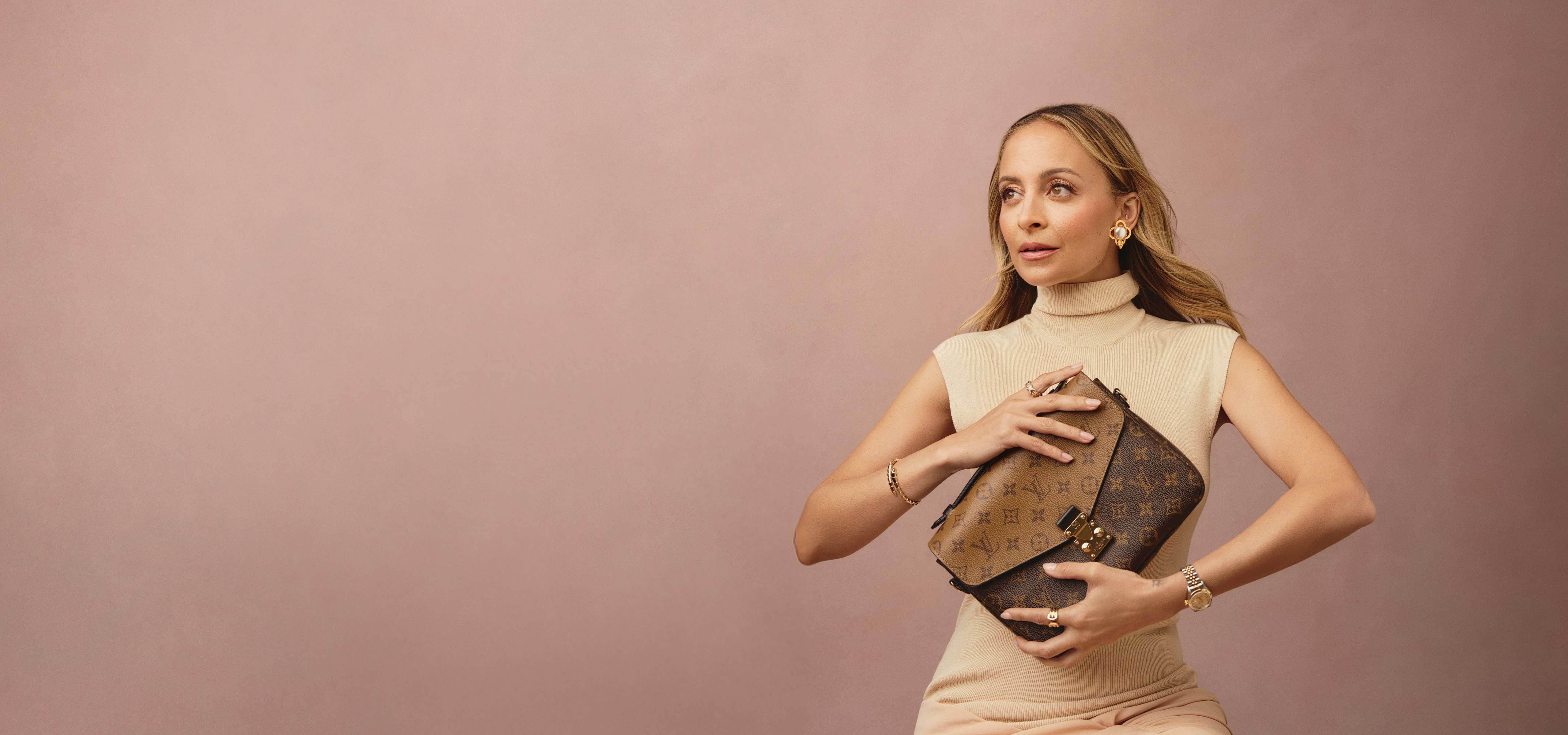 Nicole Richie wearing a beige knit turtlneck sleeveless dress and holding a Louis Vuitton reverse monogram Pochette Metis bag