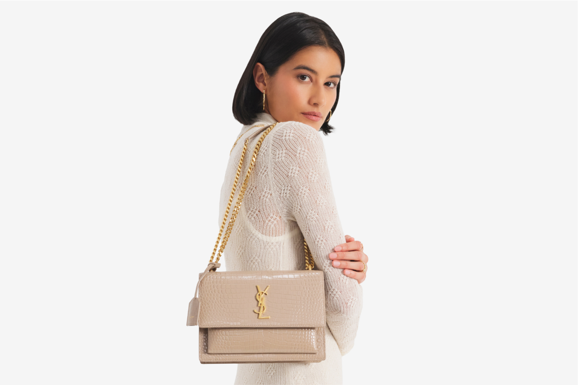 a woman wearing a white long sleeve dress and holding a beige Saint Laurent crocodile embossed Sunset chain shoulder bag with yellow gold hardware