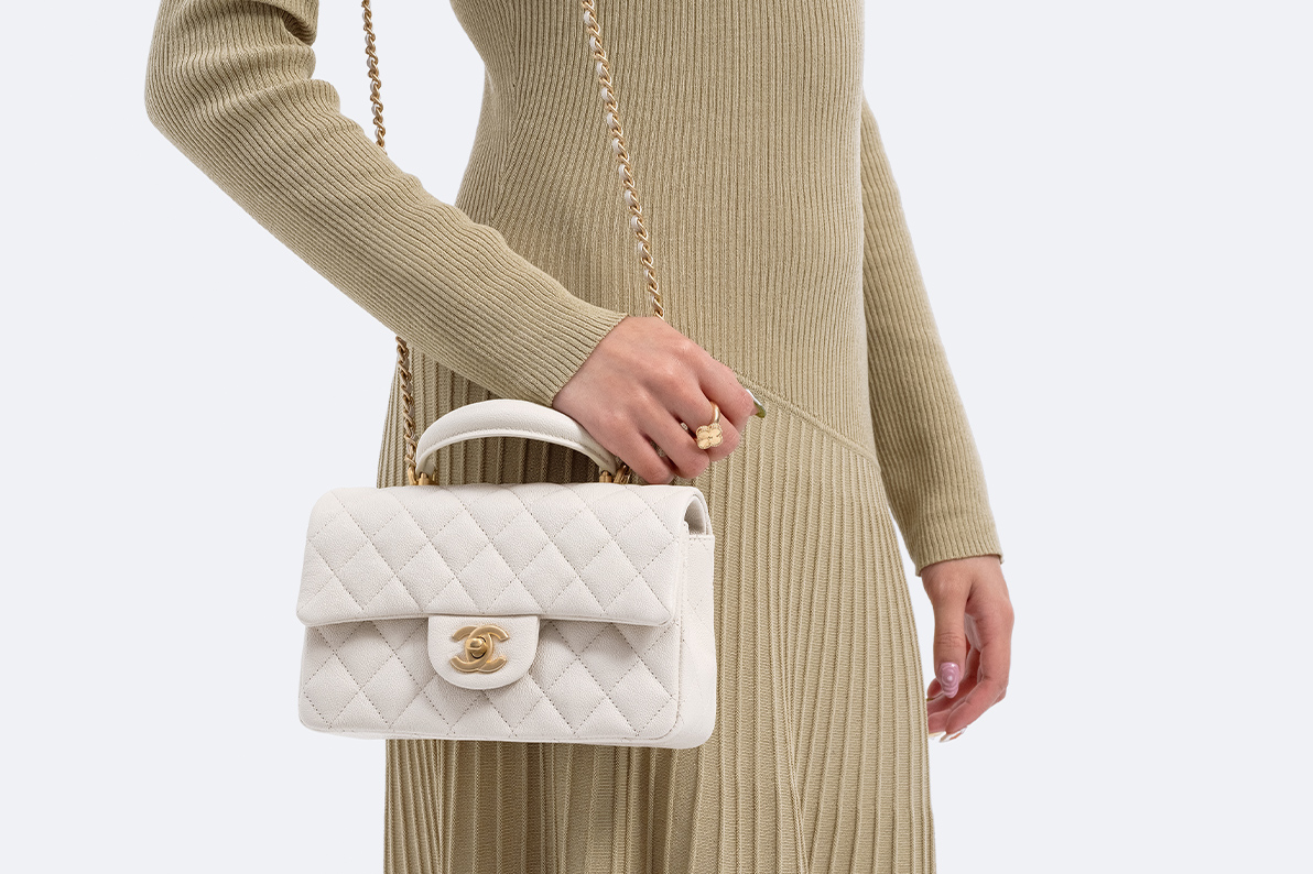 a woman wearing an olive green long sleeve dress and holding a light grey Chanel Caviar Quilted Mini Top Handle Rectangular Flap bag