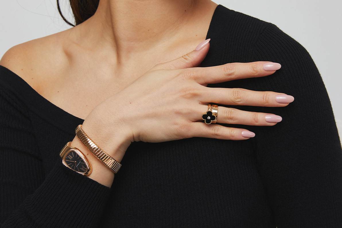 a woman in a black top wearing a BULGARI 18K Rose Gold Diamond Bezel 35mm Serpenti Tubogas Quartz Watch Black on her wrist and one VAN CLEEF & ARPELS 18K Yellow Gold Black Onyx Diamond Vintage Alhambra Ring on her finger