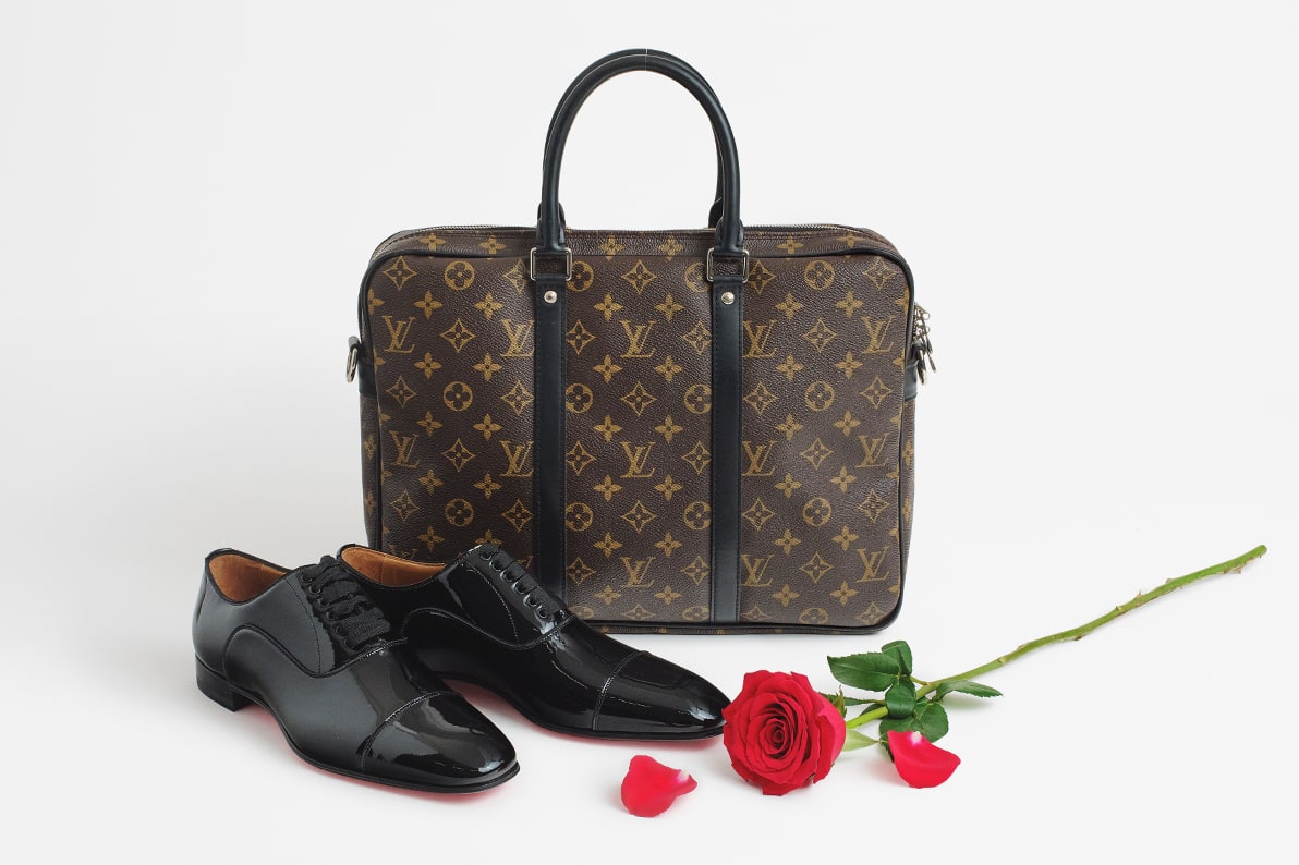 a monogram Louis Vuitton briefcase, a pair of black patent leather Christian Louboutin oxford shoes and a red rose