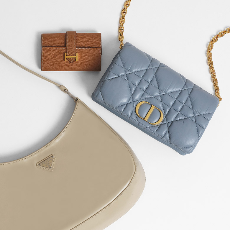 one PRADA Spazzolato Cleo Shoulder Bag Deserto lying next to one light blue CHRISTIAN DIOR Lambskin Cannage Large Caro Bag and one gold HERMES Epsom Bearn Wallet