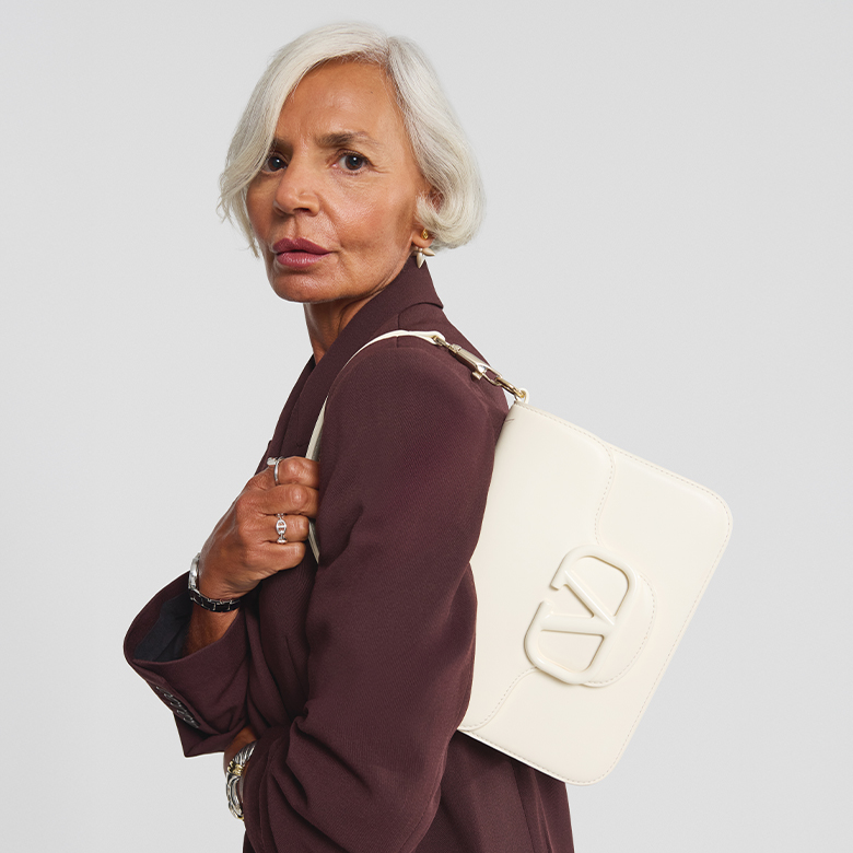 a woman in a brown suit holding a white VALENTINO GARAVANI VLogo Loco Flap Shoulder Bag 