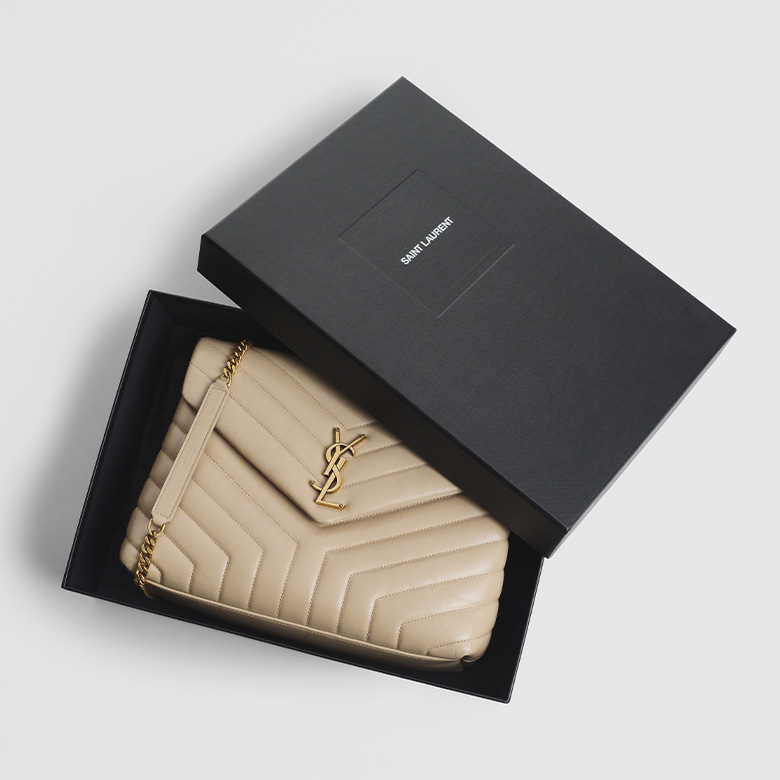 one light beige color Saint Laurent Lou bag sitting in a black Saint Laurent box with the box lid ajar over the bag