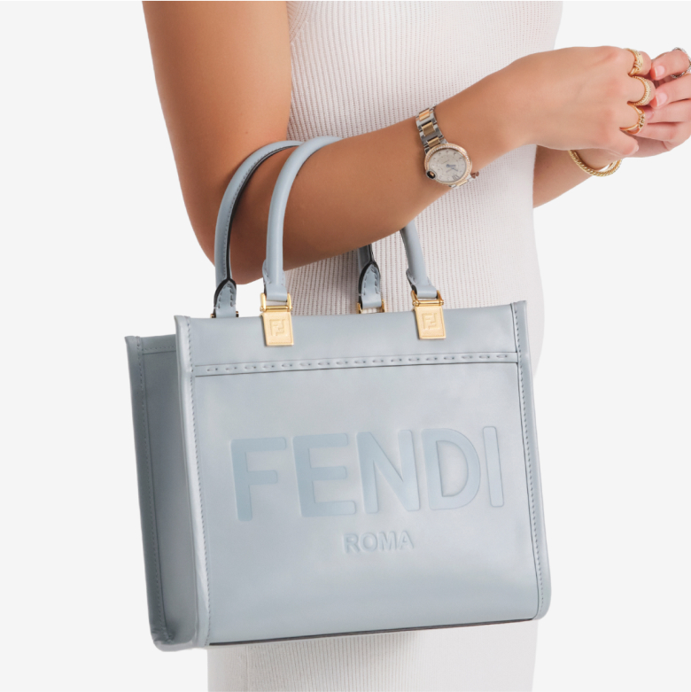 a woman in a white sleeveless dress holding a FENDI Vitello King Logo Embossed Small Fendi Sunshine Shopper Tote Anice