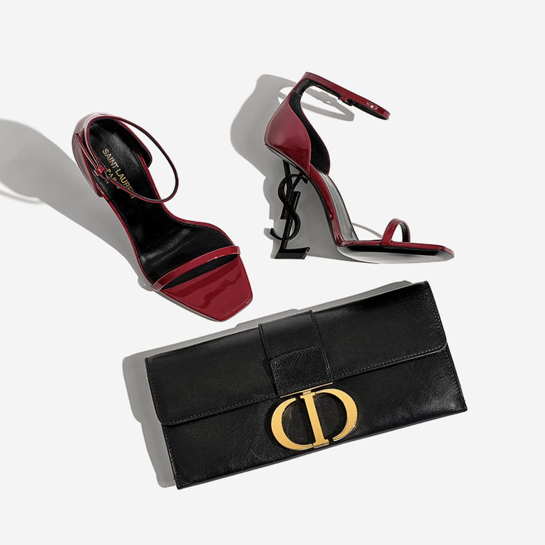 one pair of burgundy SAINT LAURENT Suede Calfskin Opyum 110 Sandals lying next to one CHRISTIAN DIOR Crinkled Lambskin 30 Montaigne Clutch