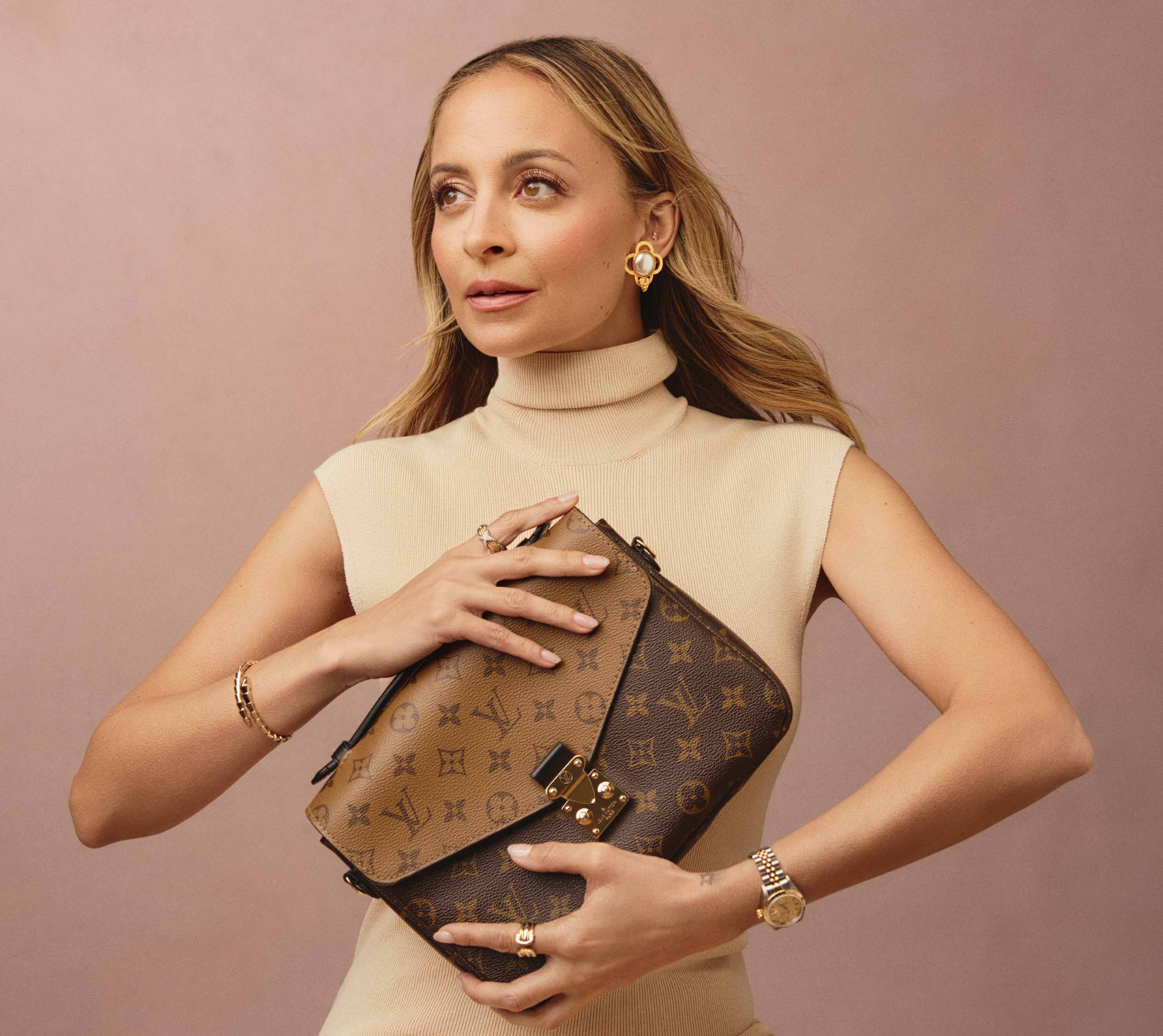Nicole Richie wearing a beige knit turtlneck sleeveless dress and holding a Louis Vuitton reverse monogram Pochette Metis bag