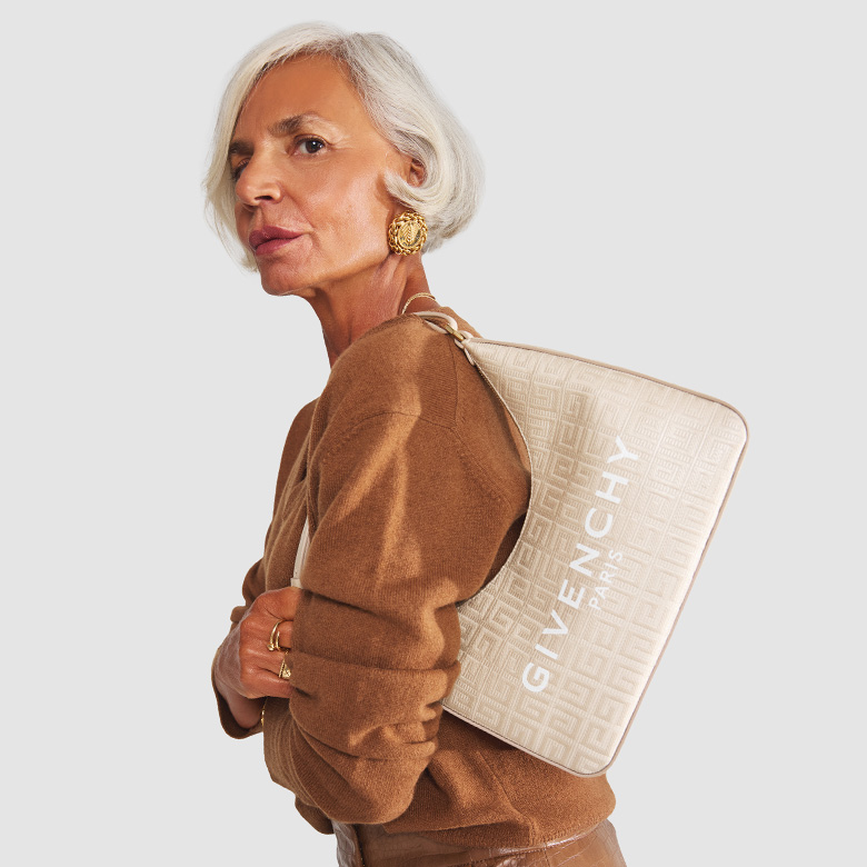 influencer Grece Ghanem wearing a tan color v-neck sweater and a tan leather midi skirt and holding a light beige Givenchy monogram shoulder bag with Givenchy logo in white on the body of the bag