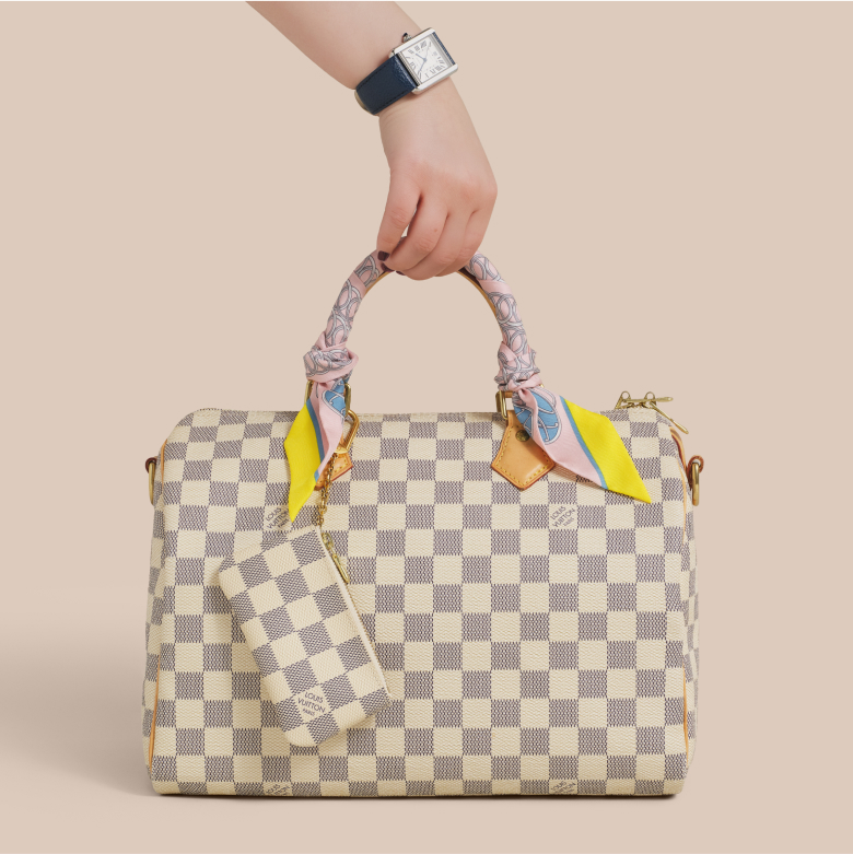 a woman wearing a blue leather strap Cartier Tank watch and holding a Louis Vuitton Damier Azur Speedy 30 with a Hermes silk Twilly scarf wrapped around the handle and a Louis Vuitton Damier Azur key pouch hanging from the handle