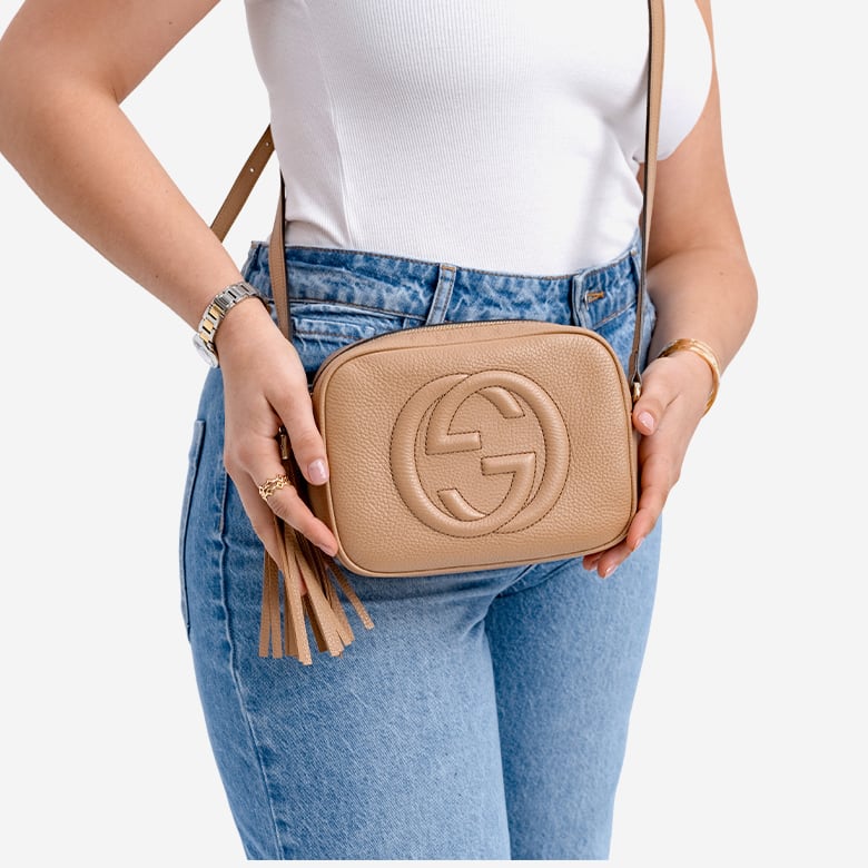 a woman in a white t shirt and denim pants holding a beige Gucci Soho bag
