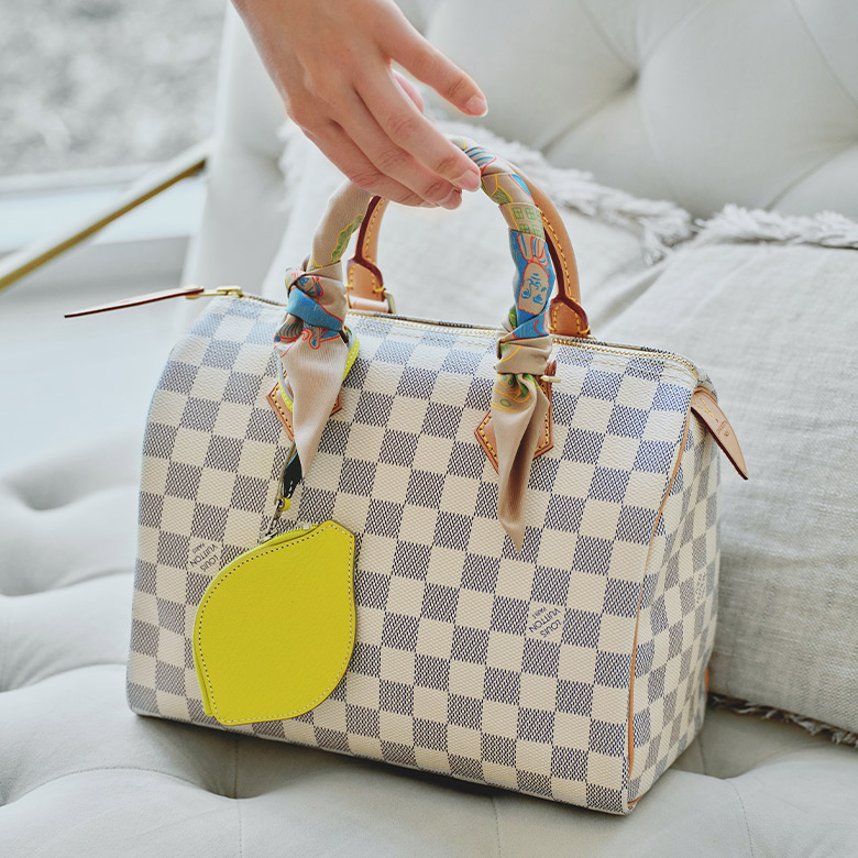one Louis Vuitton Damier Azur Speedy with a Louis Vuitton Bandeau wrapped on the handle and a HERMES Chevre Mysore Tutti Frutti Citron Coin Purse handing off the handle