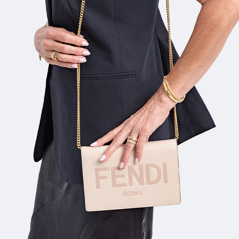 a woman wearing a black sleeveless blazer and a black sleeveless dress holding a beige Fendi wallet on chain bag