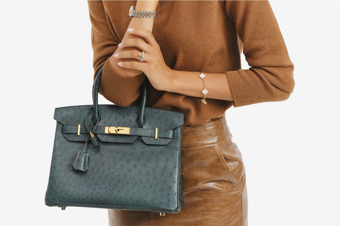 a woman wearing a tan sweater tucked into a tan leather skirt and she's holding a green ostrich Hermes Birkin 30 bag