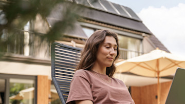 Frau am Laptop im Garten im Hintergrund Dach mit Solaranlage