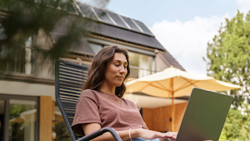 Frau am Laptop im Garten im Hintergrund Dach mit Solaranlage